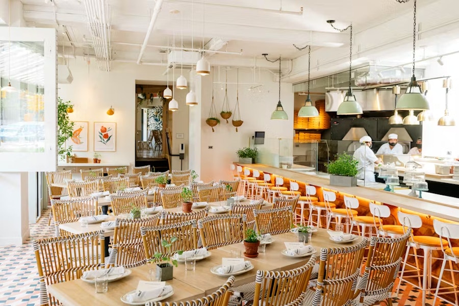 A private dining room at Rosemary's East with multiple tables set up, with a view of the pizza kitchen in the background.