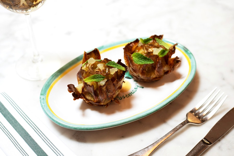 Two fried artichokes on a plate, topped with segments of lemon and mint leaves.